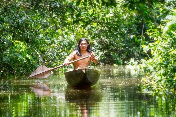 Hombre indígena en una canoa, navegando por un río en la selva.