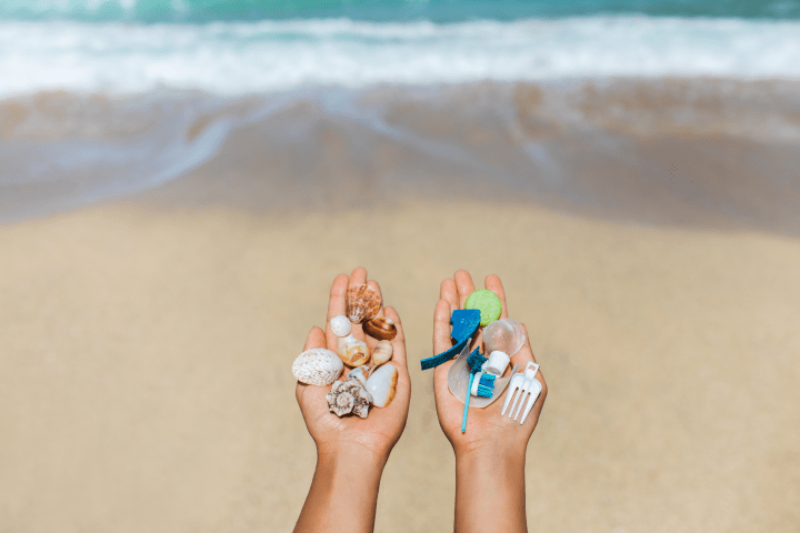 Primer plano de dos manos frente al mar, en la playa. Una mano sostiene caracoles y la otra sostiene artículos de plástico, como un tenedor y un cepillo de dientes.