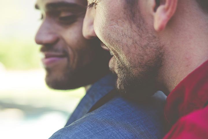 Primer plano del rostro de perfil de un hombre, que apoya el mentón sobre el hombro de otro hombre.