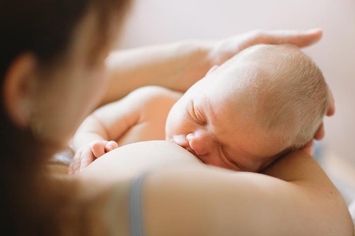 Bebé con los ojos cerrados tomando del pecho de una mujer. El rostro de la mujer está fuera de foco.