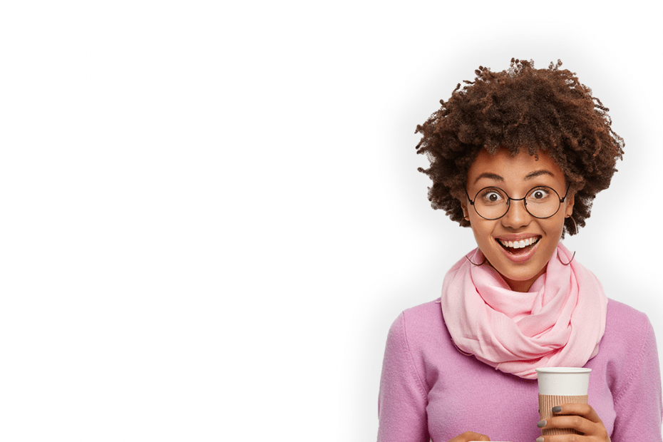 Imagen de una mujer mirando sonriente a la cámara. Sostiene en su mano derecha un dispositivo móvil y en la izquierda un café.