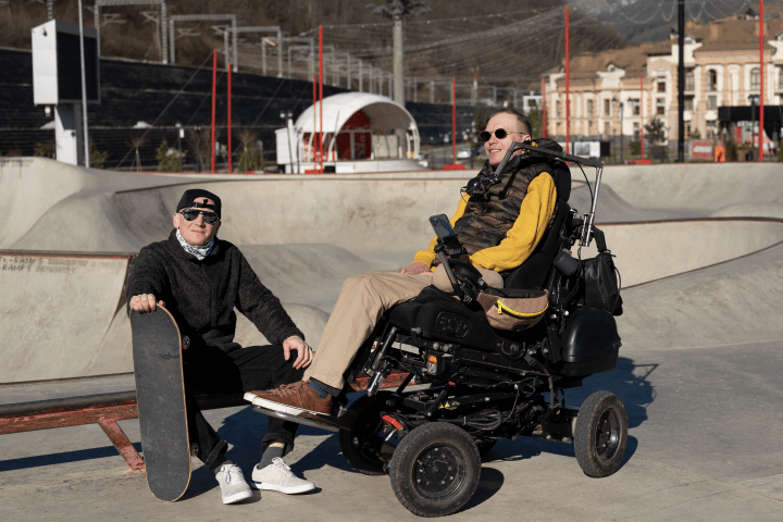 Dos hombres en un parque. Uno de los hombres está en una silla de ruedas.